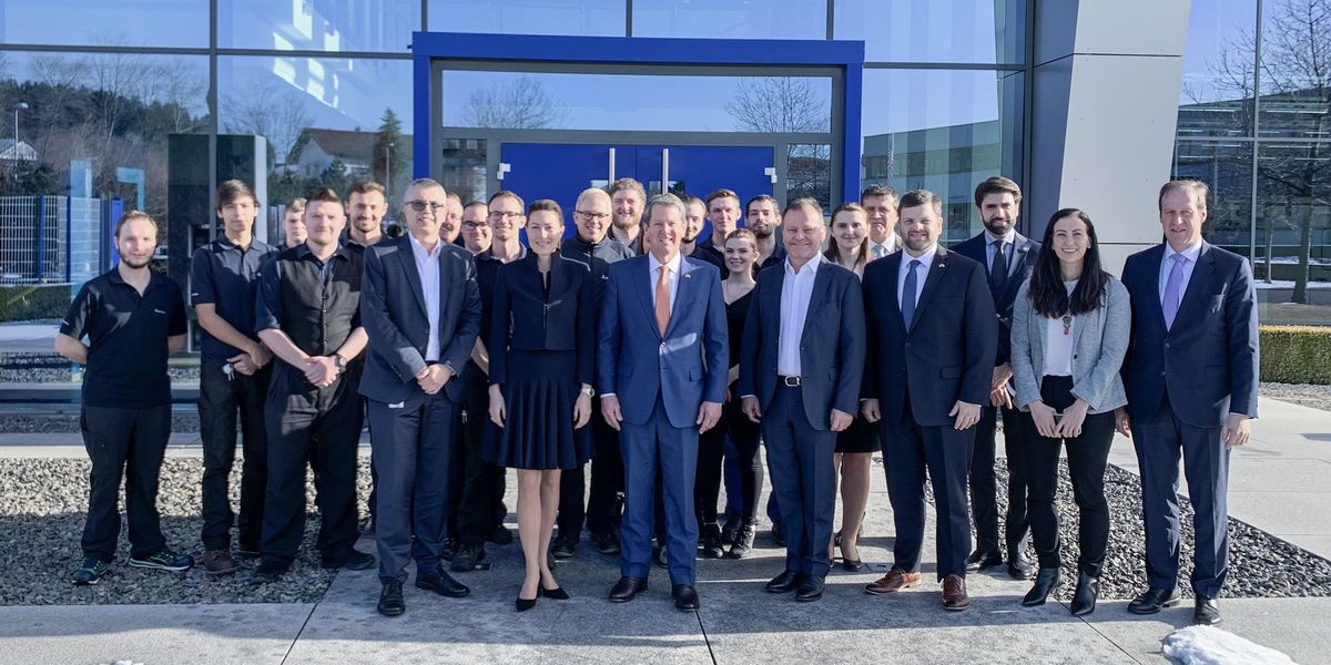 Geschäftsleitung von Häring steht mit dem Gouverneubesuch und den Mitarbeiter vor dem Gebäude von Häring und lächeln in die Kamera