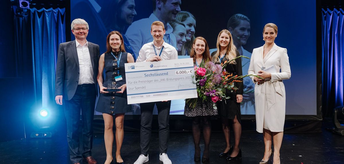 Geschäftsleitung Miriam Häring steht mit fünf weitere Personen auf der Bühne und hält den Bildungspreis 2022 in der Hand